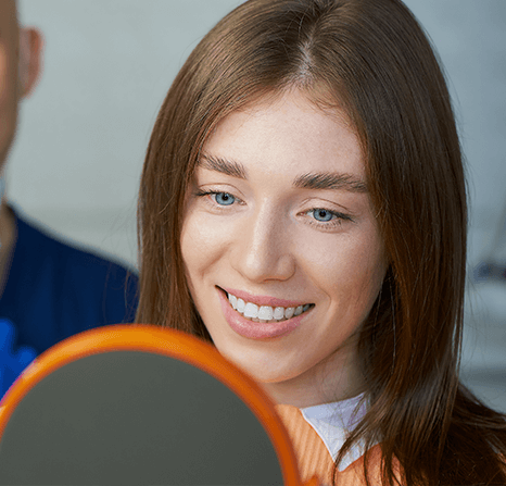 Woman looking at her smile in a mirror at the dentist.